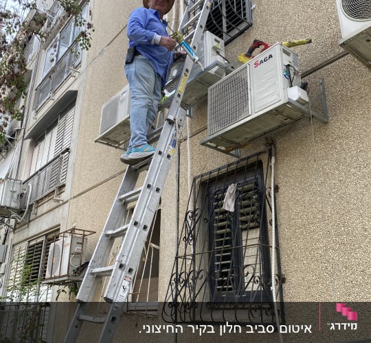 אדם על סולם עם אקדח איטום ליד מזגן